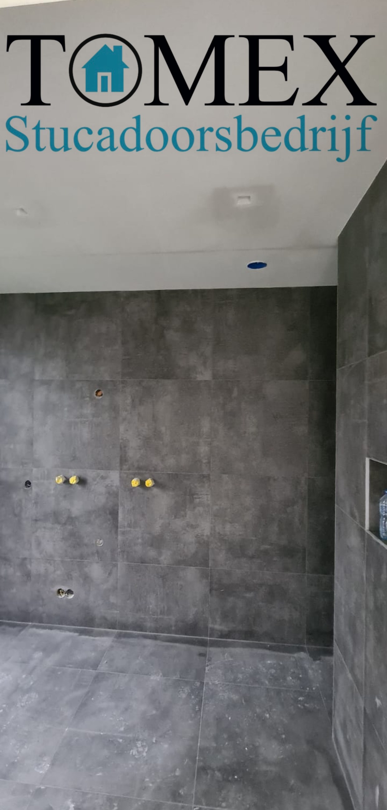 Badkamer met grote grijze wandtegels en een strak gestuct plafond