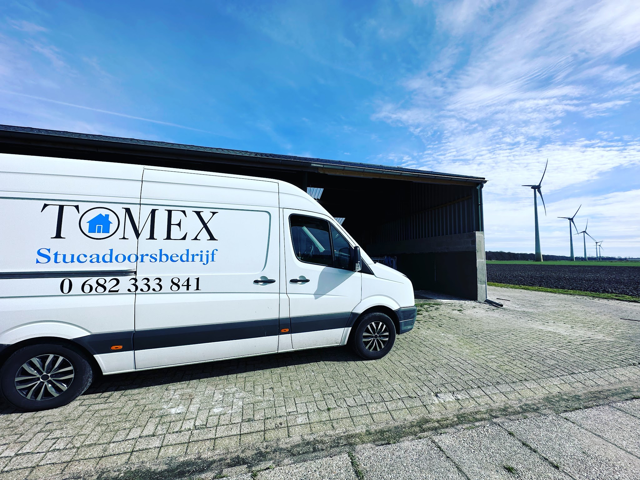 De witte bus van Tomex Stucadoorsbedrijf met logo en telefoonnummer